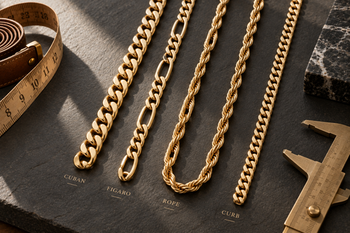 Flat lay of Cuban, Figaro, Rope, and Curb gold chain styles next to a tape measure and calipers on slate.