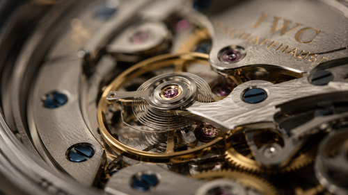 An extreme macro shot of the balance wheel and hairspring inside an IWC watch movement to show the intricate parts that require maintenance when asking how often should you service a luxury watch